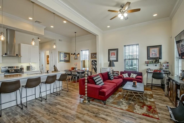 living room featuring ornamental molding, ceiling fan with notable chandelier, and light wood-type flooring