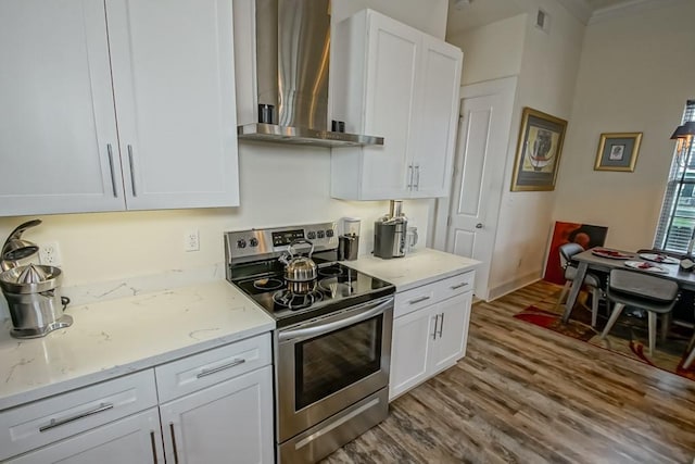 kitchen with white cabinetry, wall chimney exhaust hood, light stone counters, and stainless steel range with electric cooktop