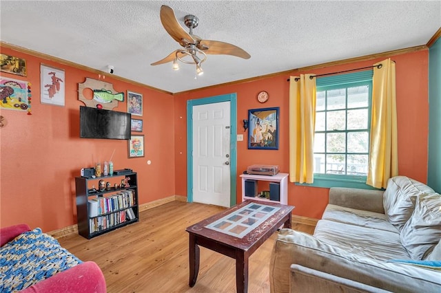 living room featuring ornamental molding, ceiling fan, a textured ceiling, and light wood-type flooring