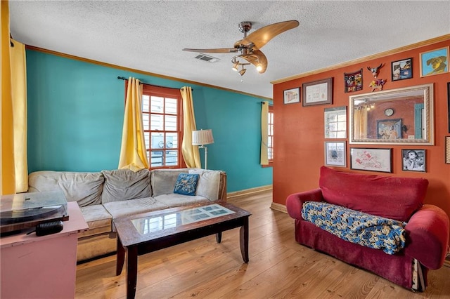 living room with ceiling fan, ornamental molding, wood-type flooring, and a textured ceiling