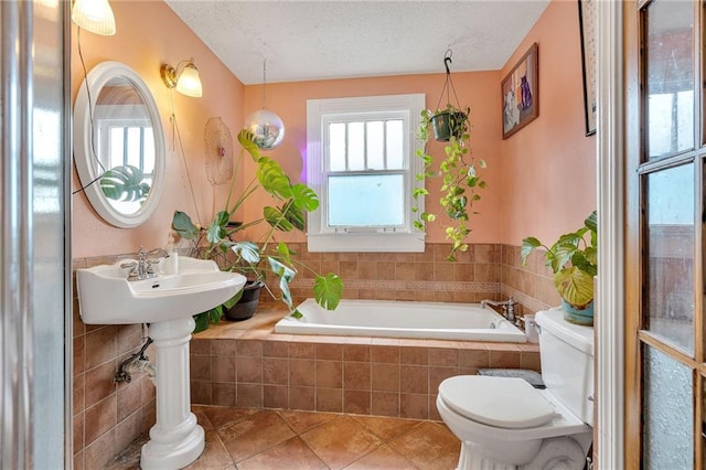 bathroom featuring a textured ceiling, tile patterned floors, tiled bath, and toilet