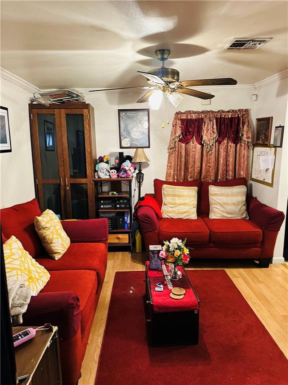 living room featuring wood-type flooring, ornamental molding, and ceiling fan