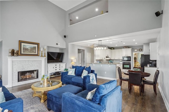 living room with a brick fireplace, dark wood-type flooring, and a high ceiling