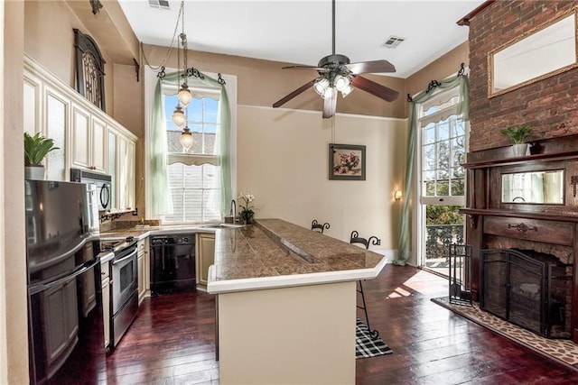 kitchen with black appliances, dark hardwood / wood-style floors, a breakfast bar area, and kitchen peninsula