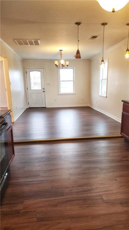 unfurnished living room featuring crown molding, plenty of natural light, an inviting chandelier, and dark wood-type flooring