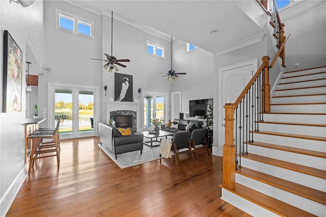 living room with hardwood / wood-style flooring, ceiling fan, ornamental molding, and a towering ceiling