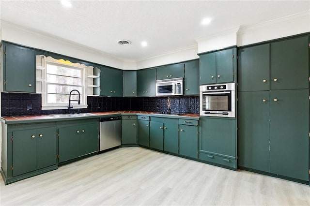 kitchen featuring sink, appliances with stainless steel finishes, ornamental molding, green cabinetry, and light wood-type flooring