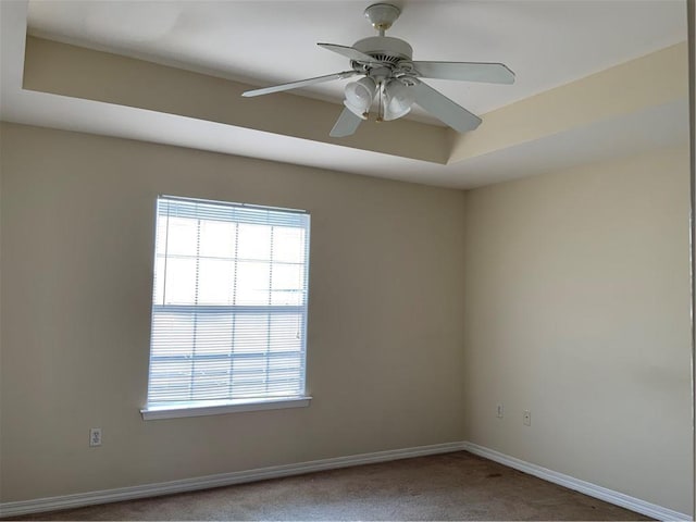 carpeted spare room with a raised ceiling and ceiling fan