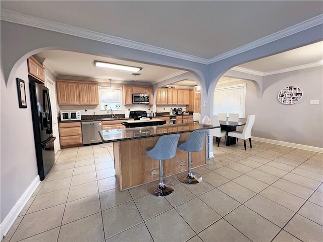 kitchen featuring light tile patterned floors, crown molding, a breakfast bar area, stainless steel appliances, and dark stone counters