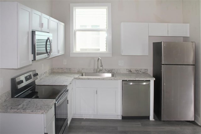 kitchen with sink, white cabinetry, light stone counters, appliances with stainless steel finishes, and dark hardwood / wood-style flooring