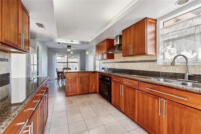 kitchen featuring a peninsula, a sink, visible vents, black appliances, and wall chimney exhaust hood