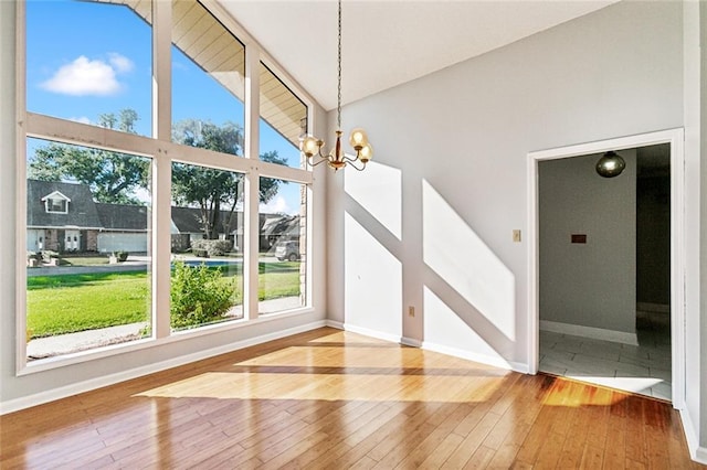 unfurnished dining area featuring a chandelier, wood-type flooring, high vaulted ceiling, and baseboards