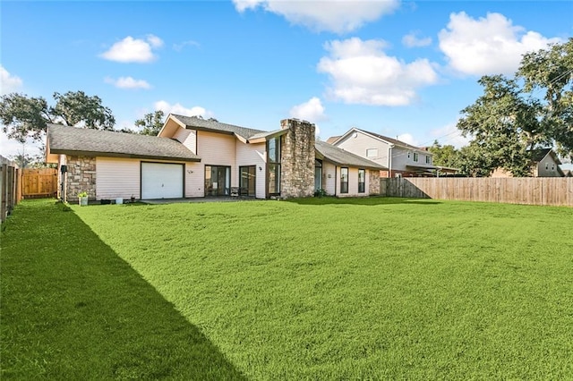 rear view of property featuring a yard, an attached garage, and a fenced backyard