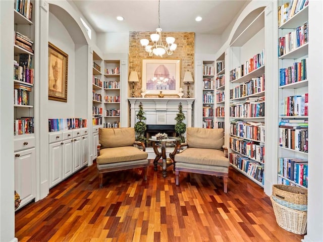 sitting room featuring a notable chandelier, bookshelves, wood finished floors, and built in features