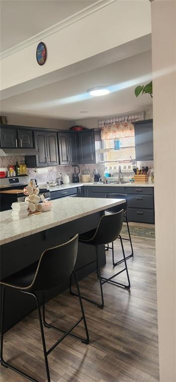 kitchen featuring sink, a breakfast bar area, hardwood / wood-style flooring, electric range, and light stone counters