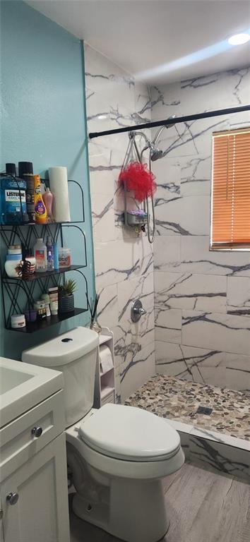 bathroom with vanity, wood-type flooring, tiled shower, and toilet