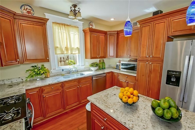 kitchen featuring hanging light fixtures, light stone countertops, sink, and appliances with stainless steel finishes