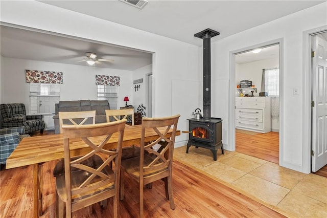 tiled dining space with ceiling fan and a wood stove