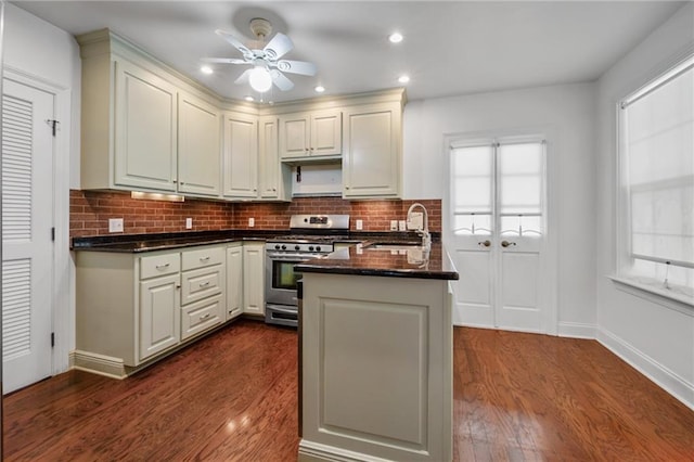 kitchen with sink, dark wood-type flooring, decorative backsplash, gas range, and kitchen peninsula