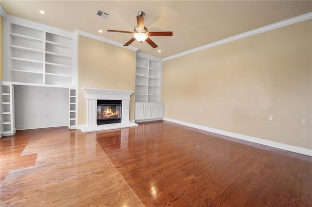 unfurnished living room with built in shelves, ceiling fan, ornamental molding, and hardwood / wood-style flooring