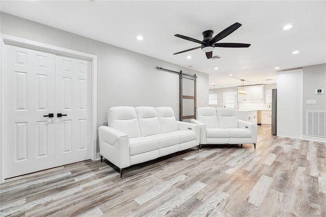 living room with a barn door, recessed lighting, light wood-style floors, and visible vents