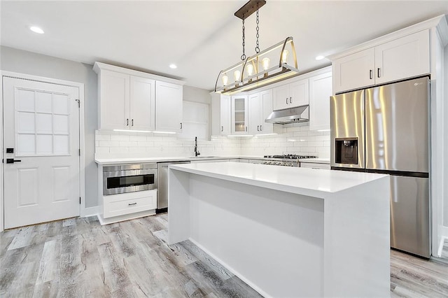 kitchen with under cabinet range hood, light wood-type flooring, appliances with stainless steel finishes, and a center island