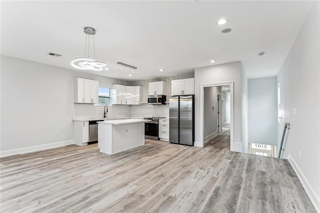 kitchen featuring appliances with stainless steel finishes, decorative light fixtures, white cabinetry, a center island, and light hardwood / wood-style floors