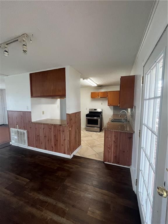 kitchen with dark hardwood / wood-style flooring, sink, wooden walls, and stainless steel range oven