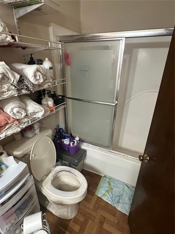 bathroom featuring parquet floors, enclosed tub / shower combo, and toilet