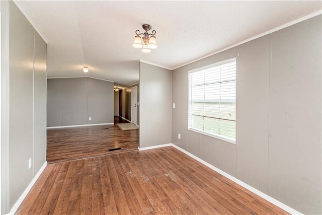 empty room featuring lofted ceiling, a notable chandelier, hardwood / wood-style flooring, and ornamental molding