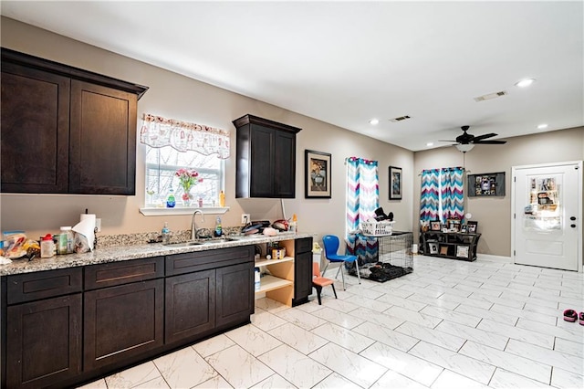 kitchen with dark brown cabinetry, sink, light stone counters, and ceiling fan