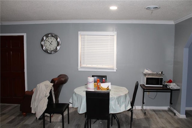 dining area featuring hardwood / wood-style flooring, ornamental molding, and a textured ceiling