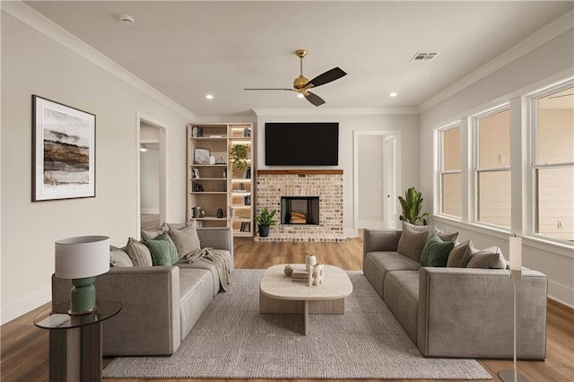 living area featuring a fireplace, wood finished floors, visible vents, a ceiling fan, and ornamental molding