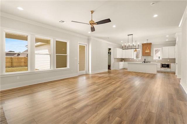 unfurnished living room with light wood finished floors, baseboards, visible vents, ornamental molding, and ceiling fan with notable chandelier