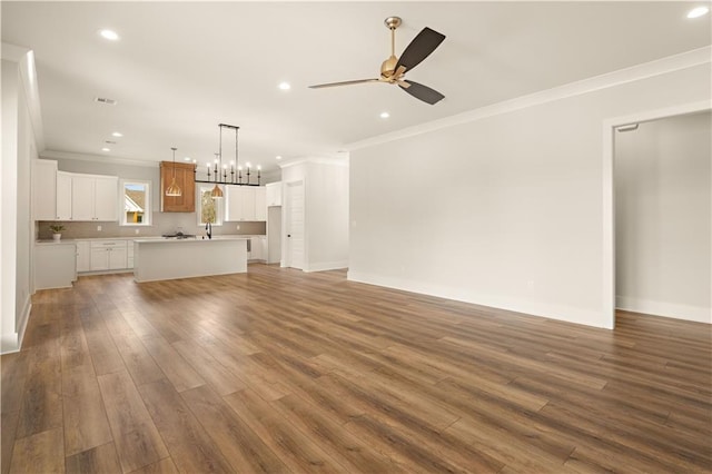 unfurnished living room with crown molding, recessed lighting, dark wood-type flooring, baseboards, and ceiling fan with notable chandelier