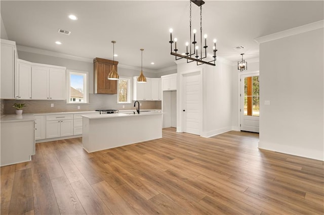 kitchen featuring a center island with sink, light countertops, hanging light fixtures, visible vents, and white cabinetry