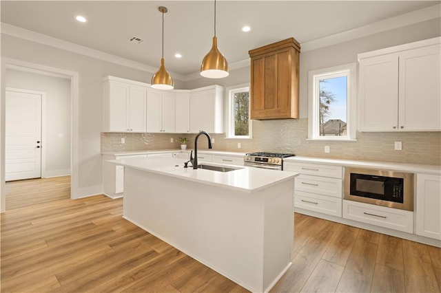 kitchen with an island with sink, light countertops, white cabinetry, black microwave, and a sink