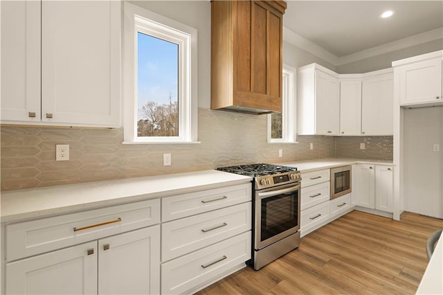 kitchen with light countertops, light wood-style flooring, white cabinets, stainless steel gas range, and built in microwave