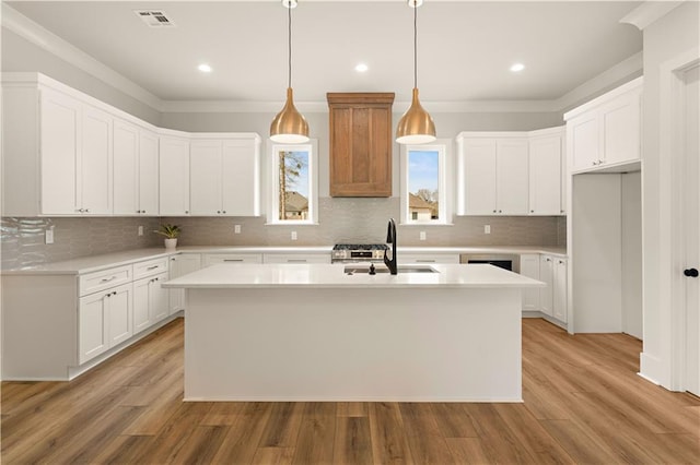 kitchen with a kitchen island with sink, visible vents, white cabinetry, light countertops, and decorative light fixtures