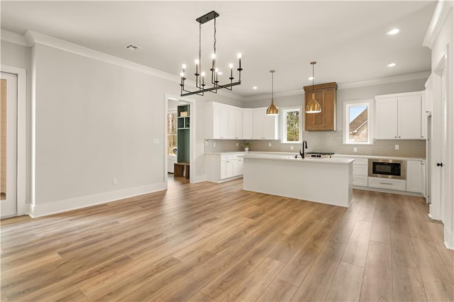 kitchen featuring black microwave, white cabinetry, light countertops, hanging light fixtures, and an island with sink