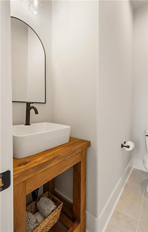 half bathroom featuring tile patterned flooring, baseboards, a sink, and toilet