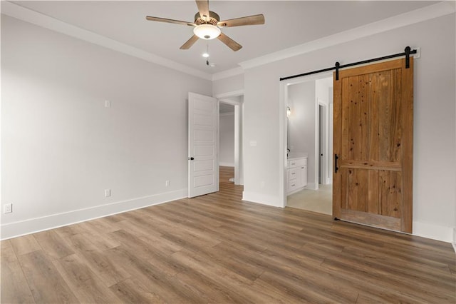 unfurnished bedroom with baseboards, a barn door, wood finished floors, and crown molding