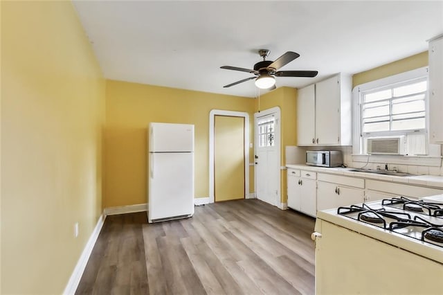 kitchen featuring white appliances, light hardwood / wood-style flooring, ceiling fan, white cabinetry, and tasteful backsplash