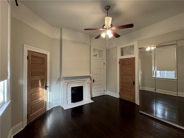 unfurnished living room featuring a fireplace with raised hearth, baseboards, wood-type flooring, and ceiling fan