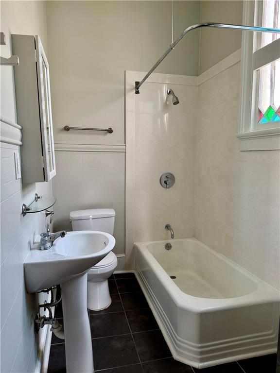 bathroom with a wainscoted wall, toilet, shower / bath combination, tile patterned floors, and tile walls