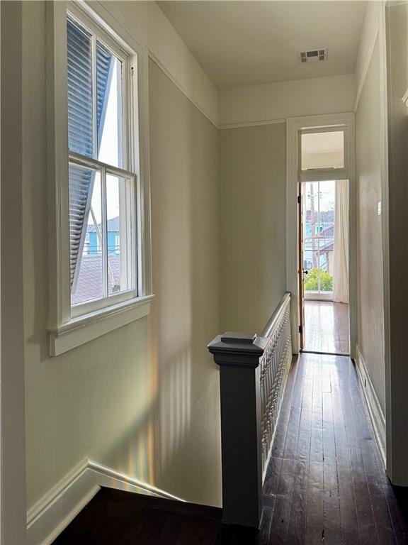 corridor with visible vents, baseboards, and dark wood-style flooring