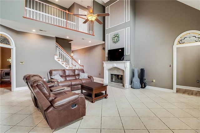 living room with a towering ceiling, a high end fireplace, ceiling fan, and light tile patterned flooring