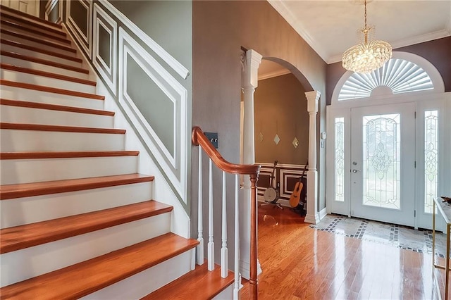 foyer entrance featuring crown molding, wood-type flooring, a chandelier, and ornate columns