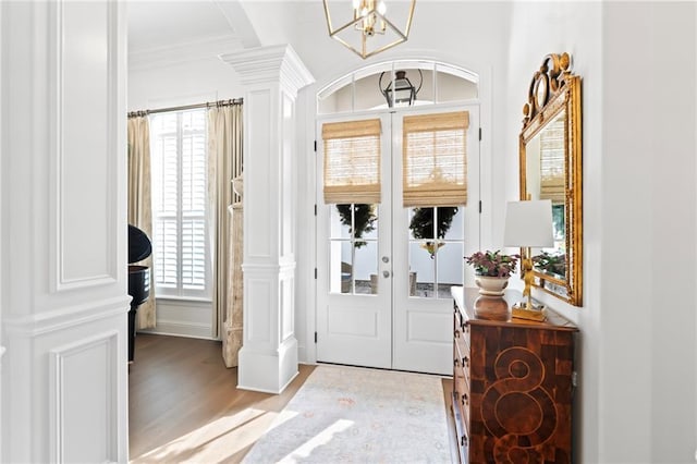 entryway featuring light hardwood / wood-style flooring, decorative columns, a notable chandelier, ornamental molding, and french doors