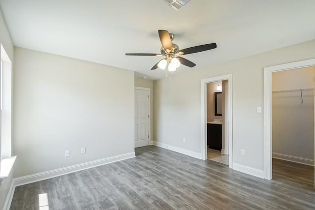 unfurnished bedroom with ensuite bathroom, a walk in closet, wood-type flooring, a closet, and ceiling fan